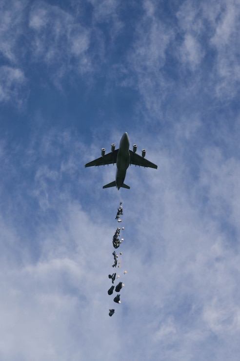 A C-17 aircraft dropping small cargo packages in the air.