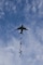 A C-17 aircraft dropping small cargo packages in the air.