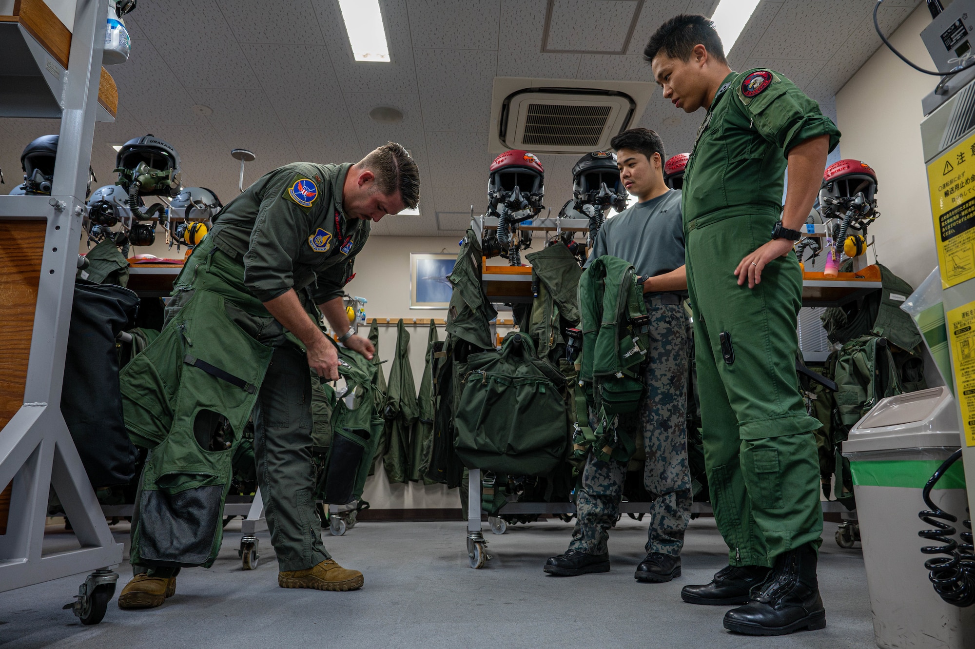 U.S. Air Force Maj. Jesse Ruter, left, weapons systems officer assigned to the 18th Operations Group, dons flight gear with the help of Japan Air Self-Defense Force members ahead of a joint training mission with JASDF pilots at Naha Air Base, Japan, Nov. 19, 2025. The mission was an opportunity for both forces to compare tactics, procedures and aircrew equipment processes up close. (U.S. Air Force photo by Airman Nathaniel Jackson)