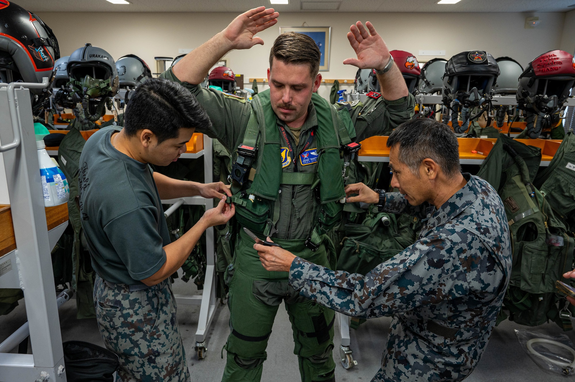 U.S. Air Force Maj. Jesse Ruter, center, weapons systems officer assigned to the 18th Operations Group, dons flight gear with the help of Japan Air Self-Defense Force members ahead of a joint training mission with JASDF pilots at Naha Air Base, Japan, Nov. 19, 2025. The mission was an opportunity for both forces to compare tactics, procedures and aircrew equipment processes up close. (U.S. Air Force photo by Airman Nathaniel Jackson)