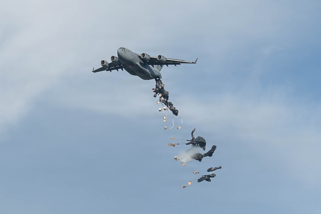A C-17 aircraft delivers cargo over a drop zone.