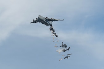 A C-17 aircraft delivers cargo over a drop zone.