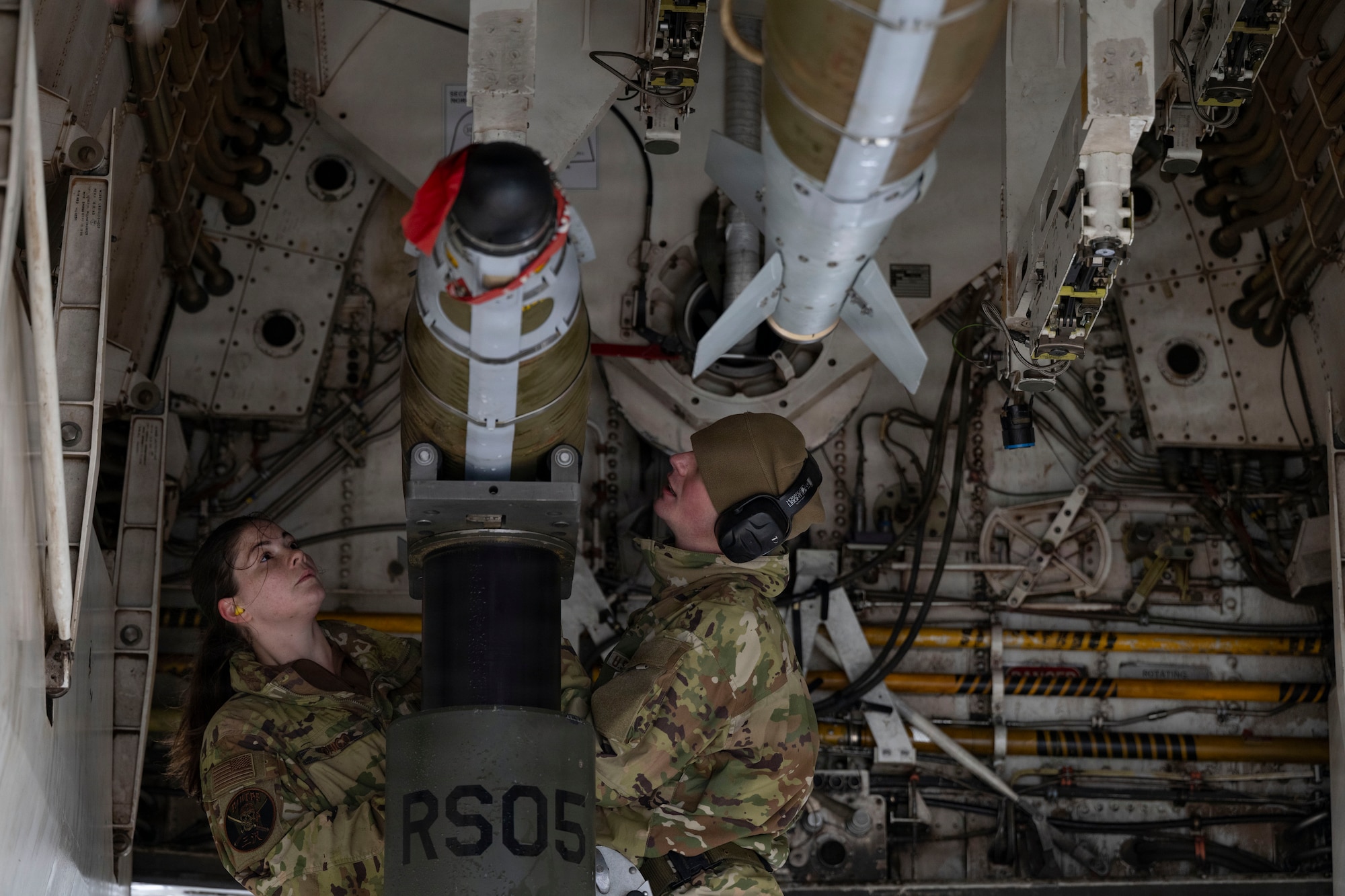 Airmen prepare to load a large weapon onto a B-1 Lancer outside on the flightline