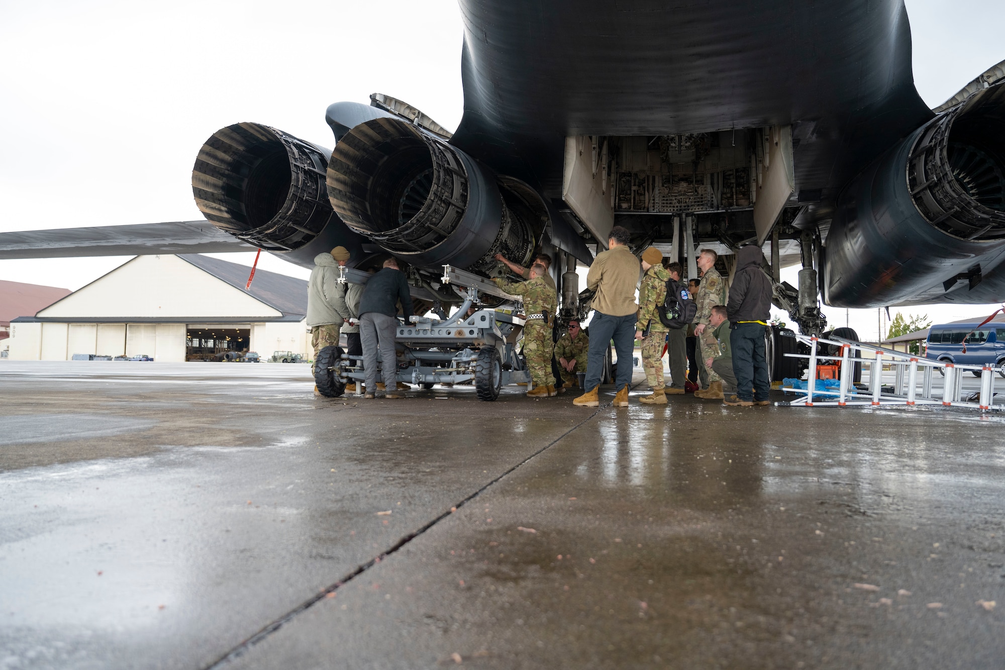 Airmen conduct maintenance on a B-1 Lancer outside in the daylight after raining outside