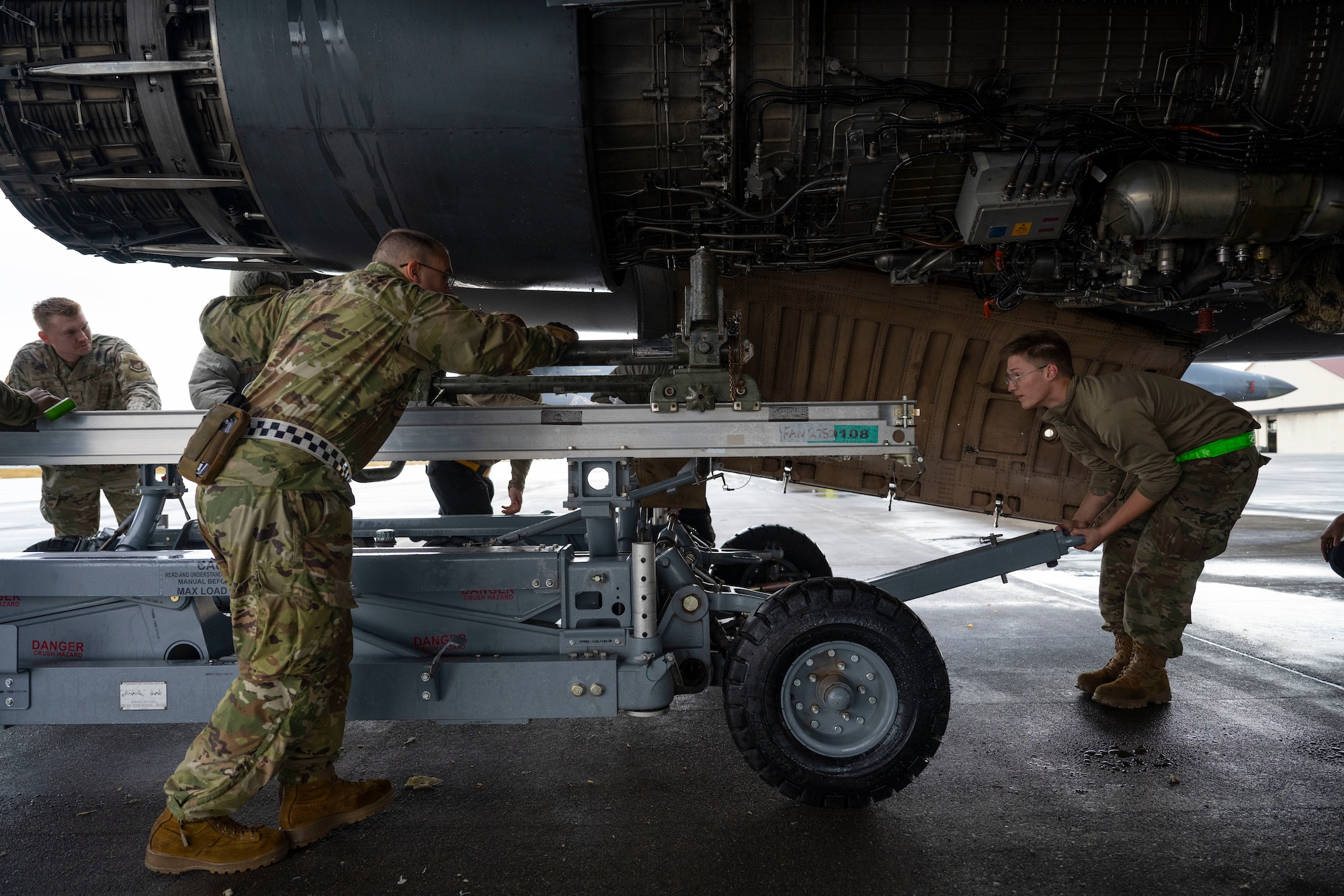 Airmen conduct maintenance on a B-1 Lancer outside in the daylight after raining outside