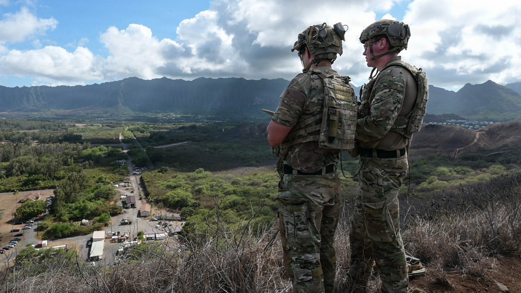 Two Airmen stand on a peak, participating in simulated airstrike training.