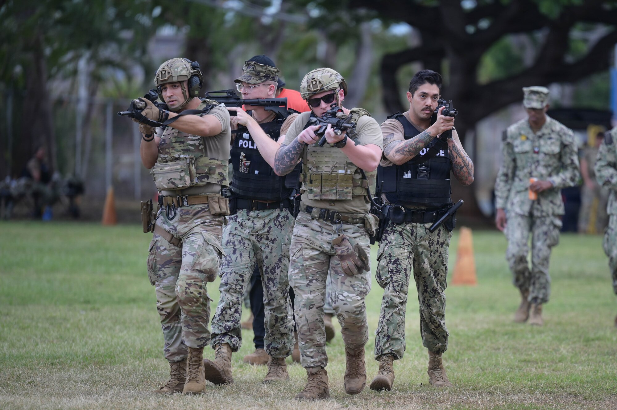 Airmen and Sailors walk in formation with rifles at the ready position during an exercise.
