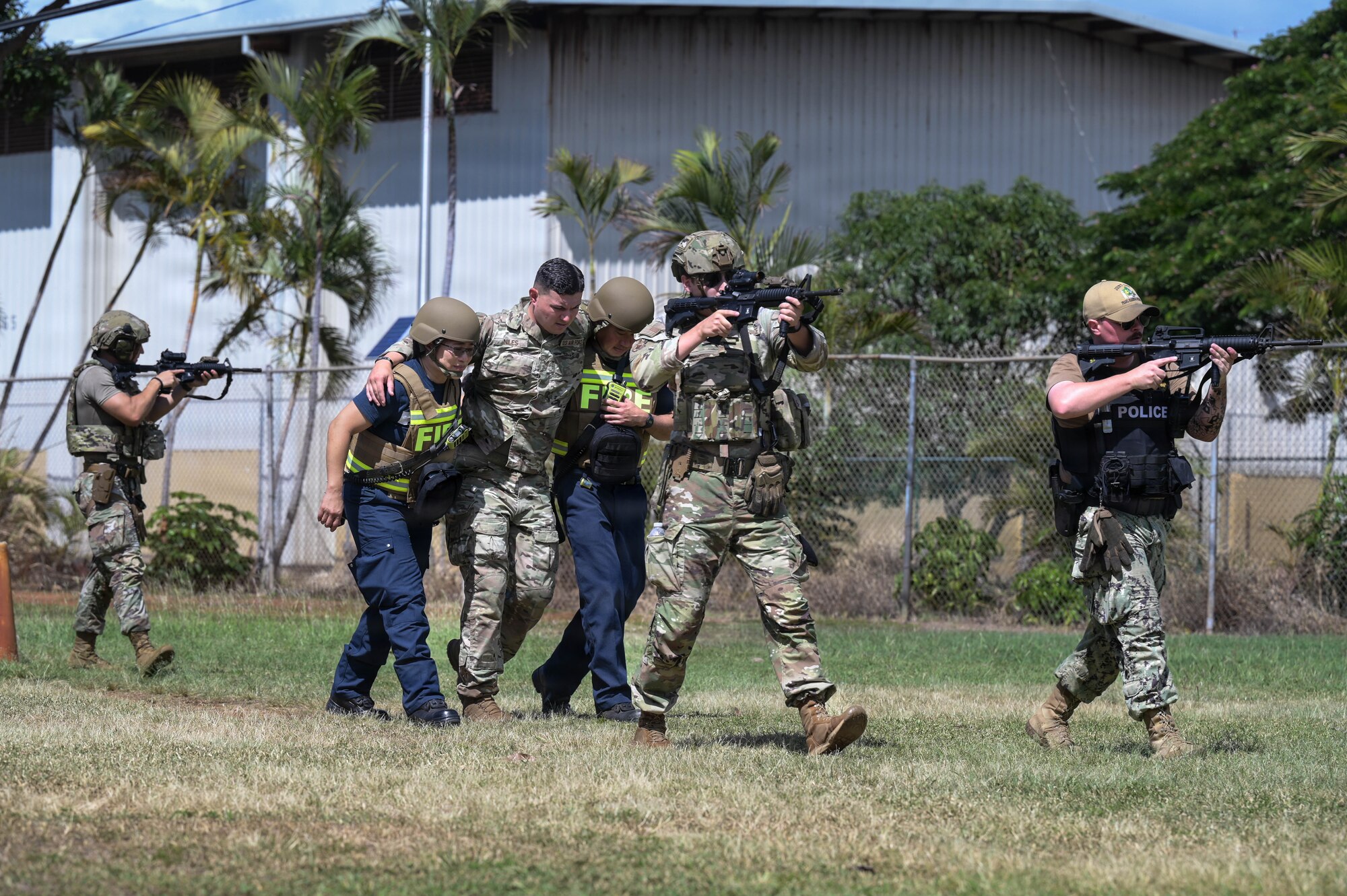 Airmen, Sailors, and firefighters walk in formation and carry a simulated patient during an exercise
