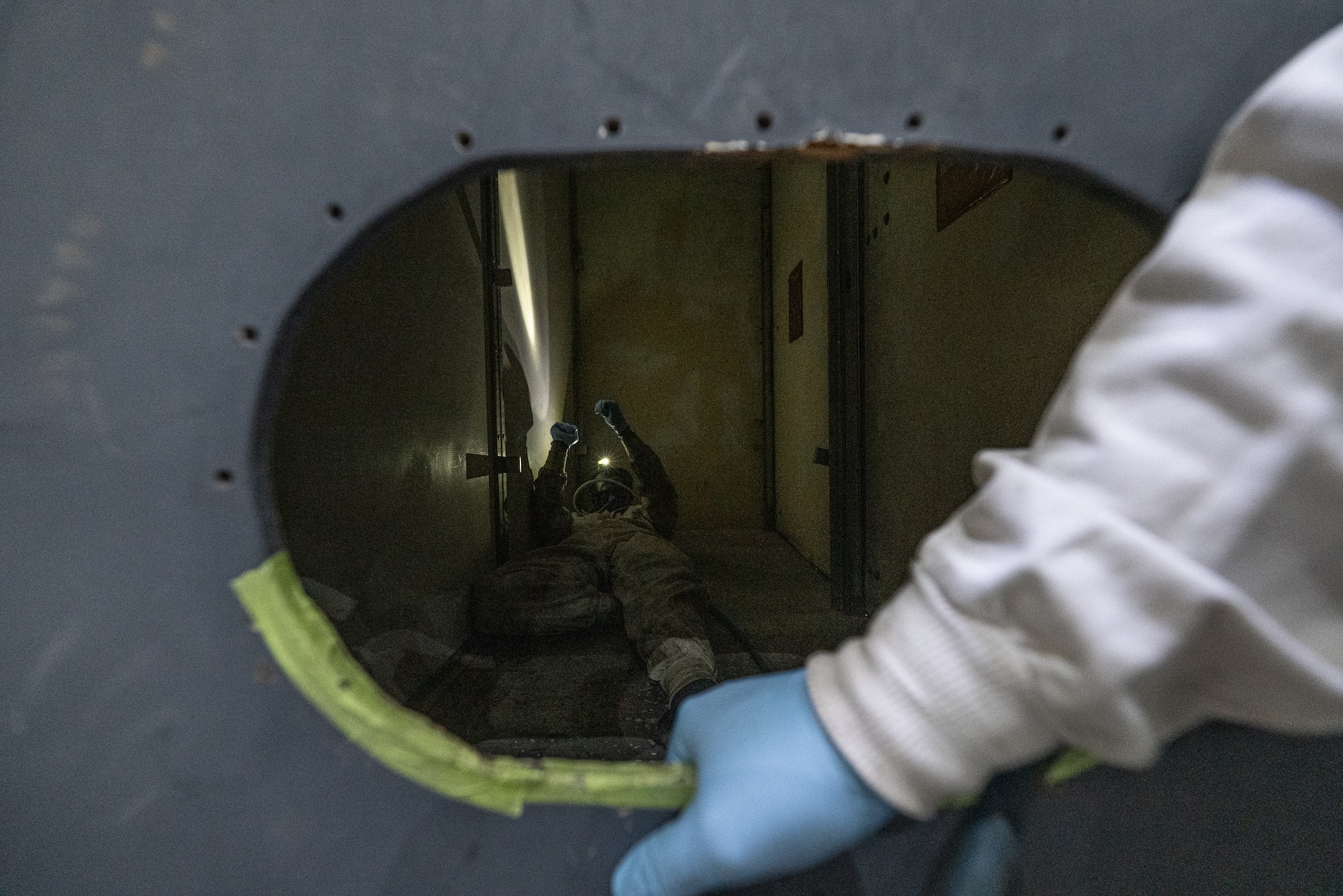 A hole fills the frame. Inside the hole an Airman is lying down feigning distress.