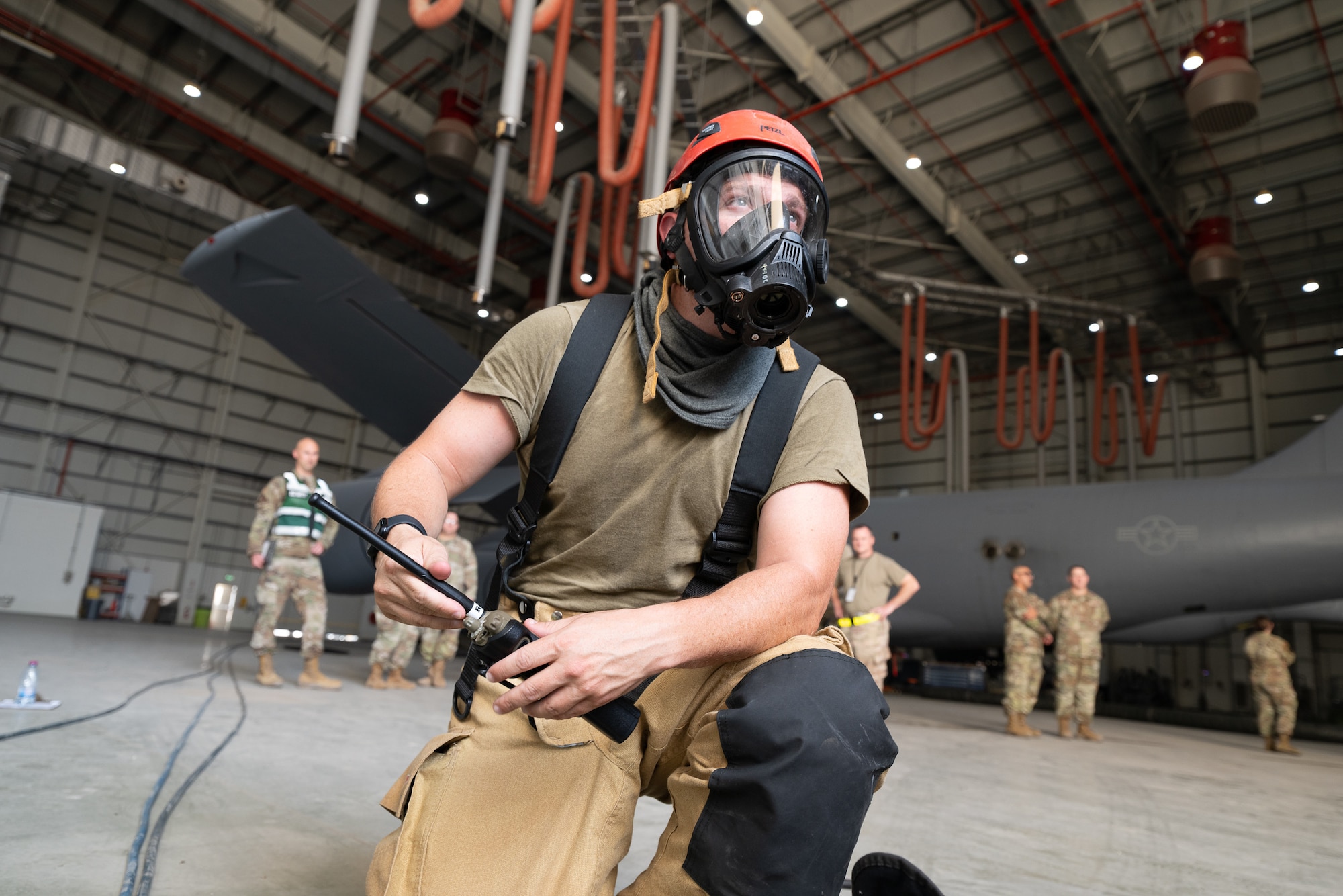 A firefighter wearing a mask kneels while holding a radio
