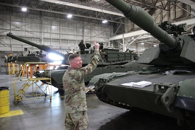 An Army soldier stands with tanks.