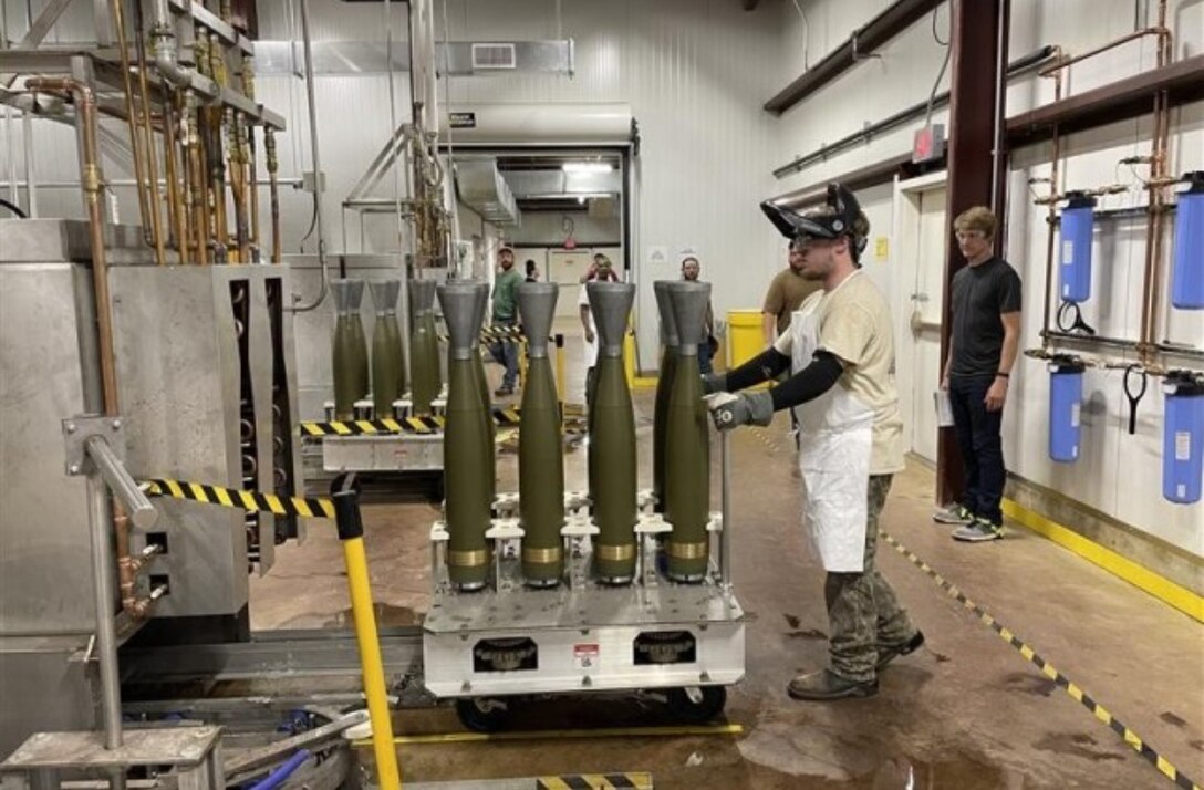 A man in an arsenal with four M795 projectiles.