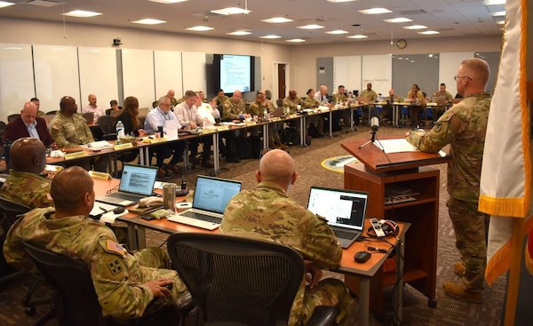 Soldiers from the Army Contracting Command sit around a table in a classroom.