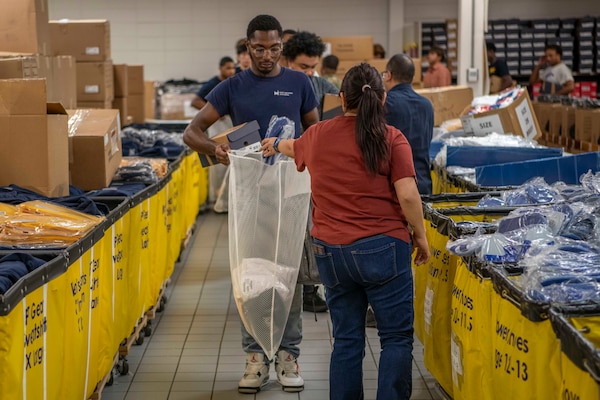 Navy recruits hold out bags to get their first uniforms