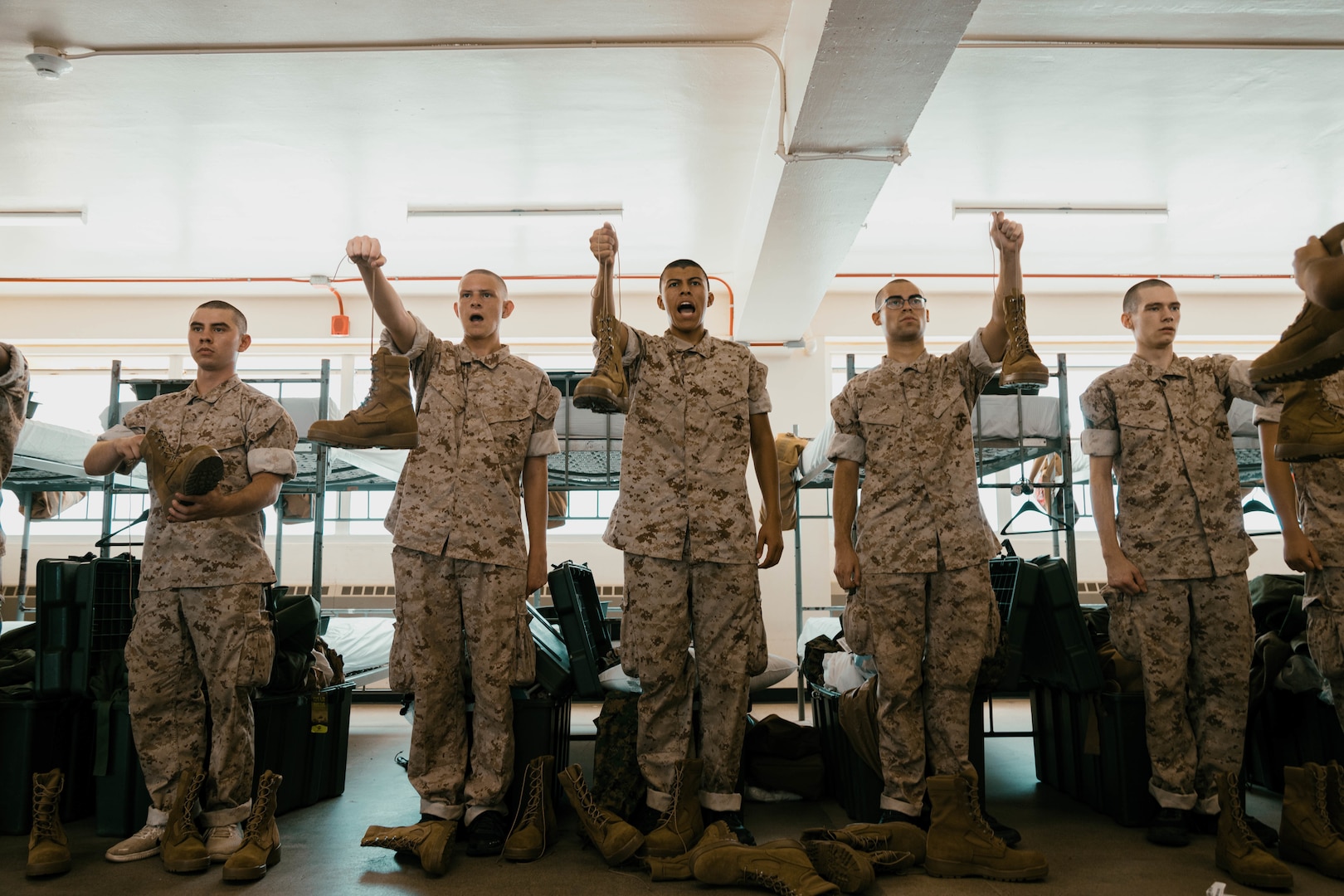 A group of Marine recruits hold up their boots for inspection.
