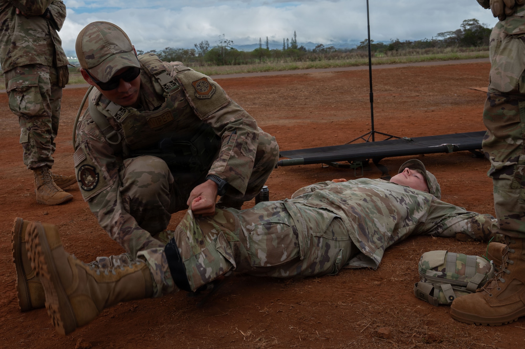 U.S. Air Force Senior Airman Justin Nieves, 21st Combat Air Base Squadron heating, ventilation, air conditioning and refrigeration technician, applies a tourniquet on Senior Airman Evan Bland, 21st CABS vehicle mechanic, as part of Casualty Collection Point training during Joint Pacific Multinational Readiness Center 26-01 at Schofield Barracks, Hawaii, Nov. 6, 2025. During JPMRC 26-01, the 21st Air Task Force and 21st CABS executed operations as part of their 300-level training within the Air Force Force Generation cycle, designed to certify their ability to deploy, establish operations, and sustain combat  airpower under contested conditions. (U.S. Air Force photo by Senior Airman Alondra Cristobal Hernandez)