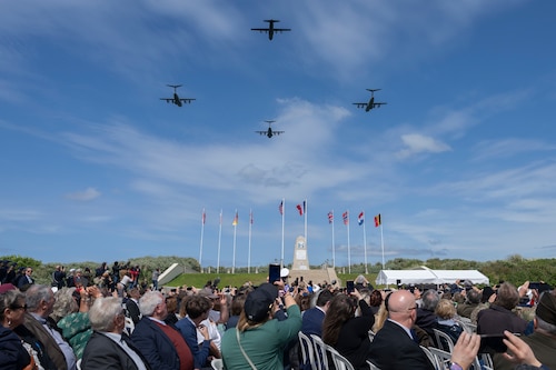 A group of people watch as four planes fly overhead in formation.