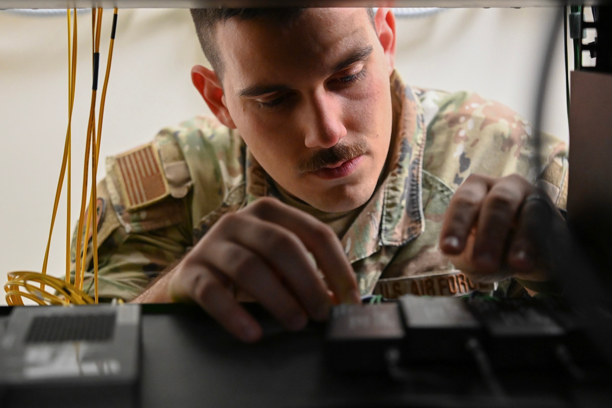 A uniformed service member reaches his hands and peers into a shelf with server connection sources.