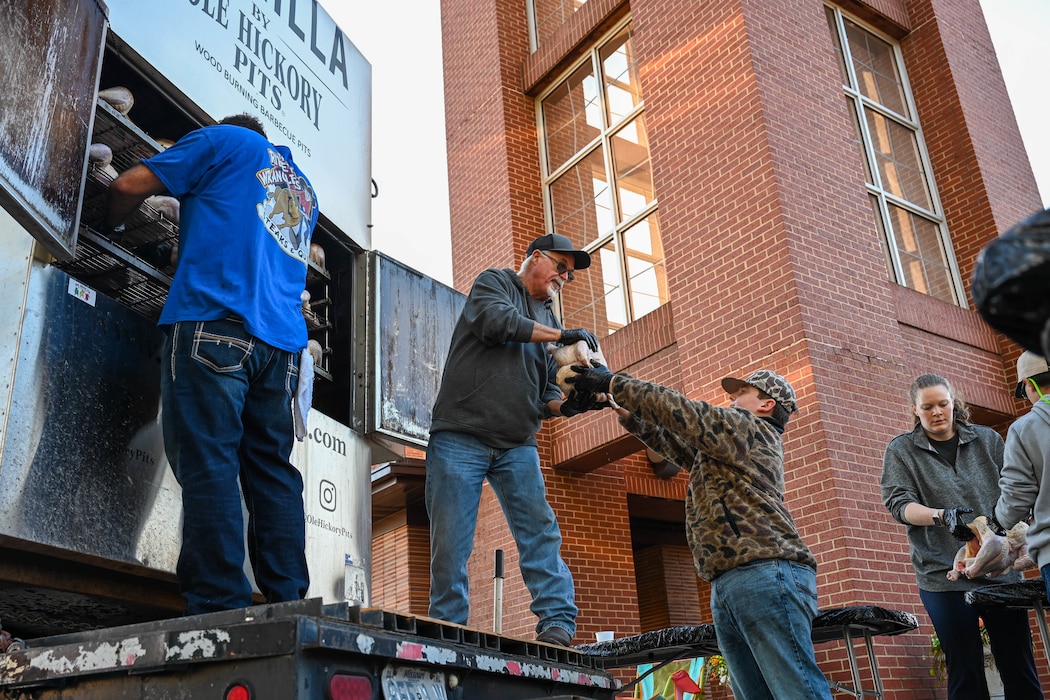 People are putting turkeys into a barbeque smoker.