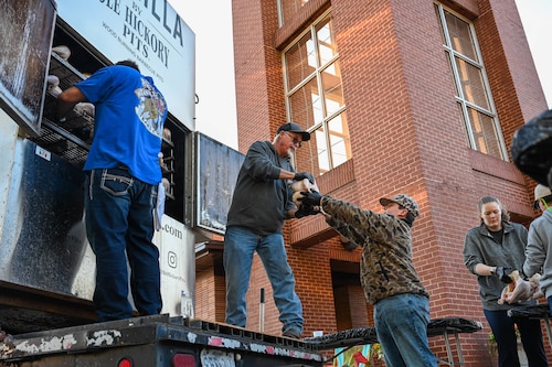 People are putting turkeys into a barbeque smoker.