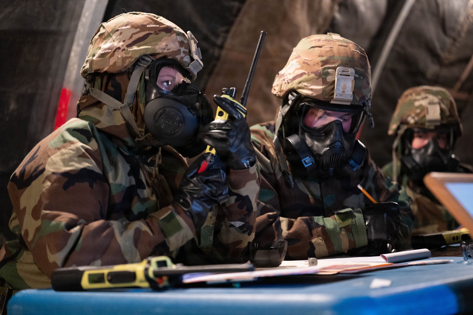 Photo of an Airman dressed in Mission Oriented Protective Posture (MOPP) gear speaking on a mobile radio.