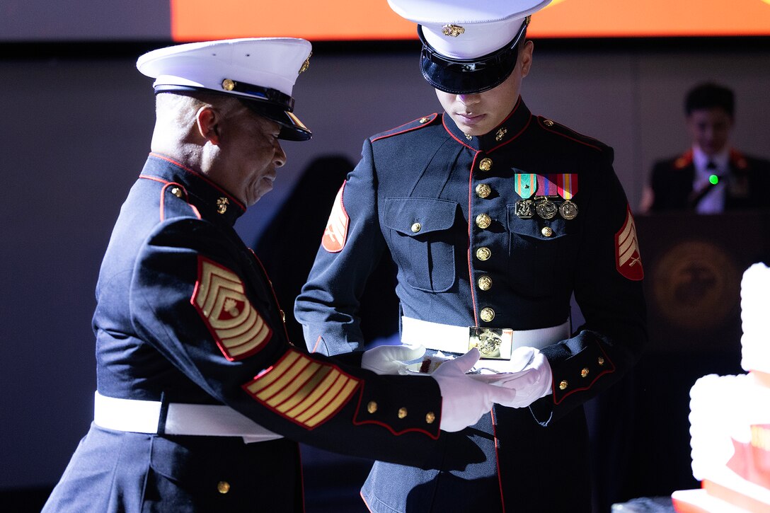 The oldest Marine present, James Whitlow, 70, a retired master gunnery sergeant with 33 years of service, passes a piece of cake to the youngest Marine present, Sgt. Bryan McDougall, 21, of Coral Springs, Florida, during the 250th Marine Corps birthday ball ceremony hosted Nov. 21 by Blount Island Command at Deerwood Castle in Jacksonville, Florida. The exchange symbolizes the passing of experience and knowledge from one generation of Marines to the next. (Official Marine Corps photo by Dustin Senger)