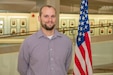 A person poses for a photo next to an American flag
