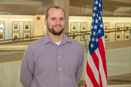 A person poses for a photo next to an American flag
