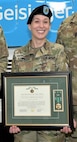 A person poses for photo wearing a military uniform and holding a plaque.