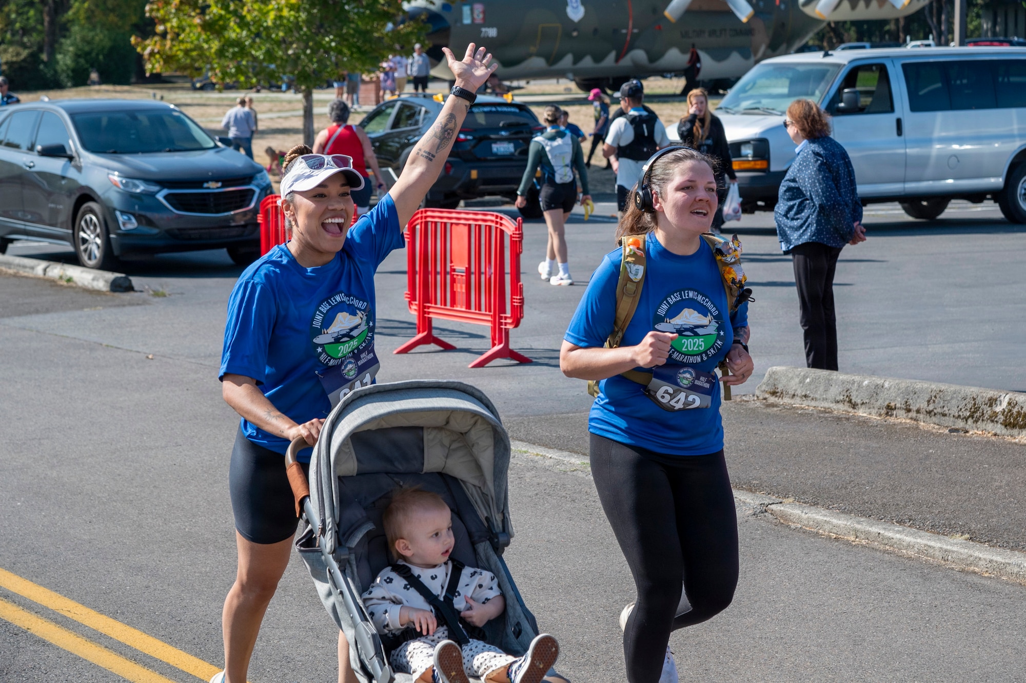 two marathon runners run side by side finish line, one is pushing a baby in a stroller