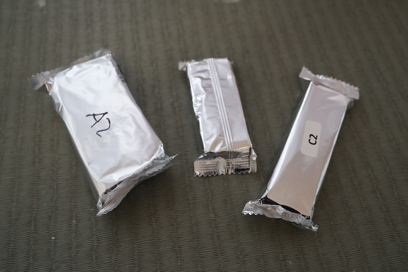 Three bar-sized food items wrapped in foil packaging sit on a table.