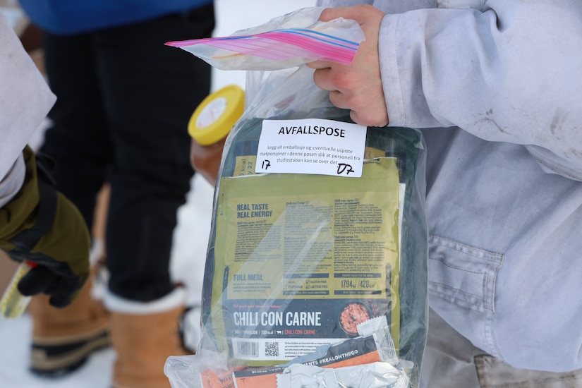 A person holds a clear plastic bag filled with pouches of food.