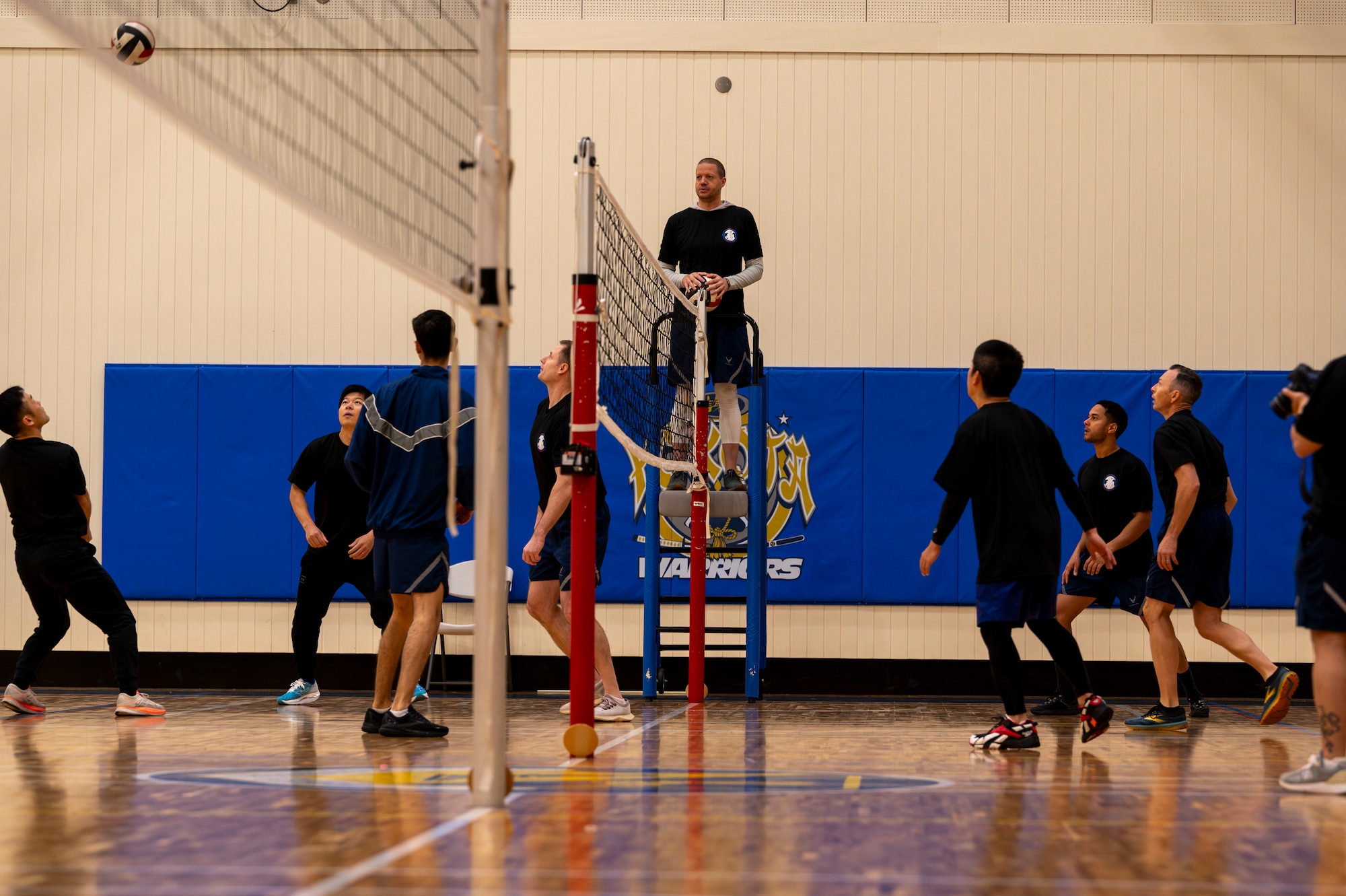 Military members in pt gear play volleyball.
