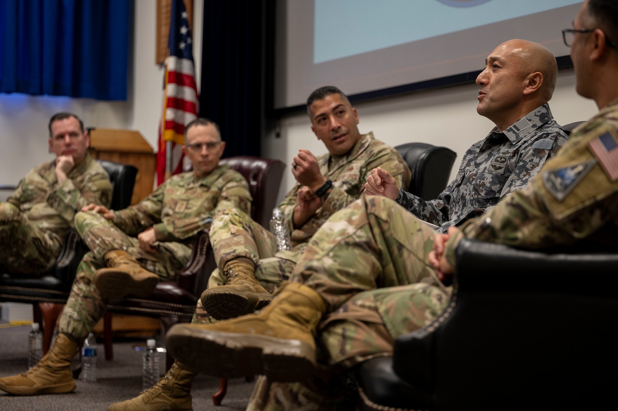 Four U.S. military members sit in chairs listening to a JASDF member speak.