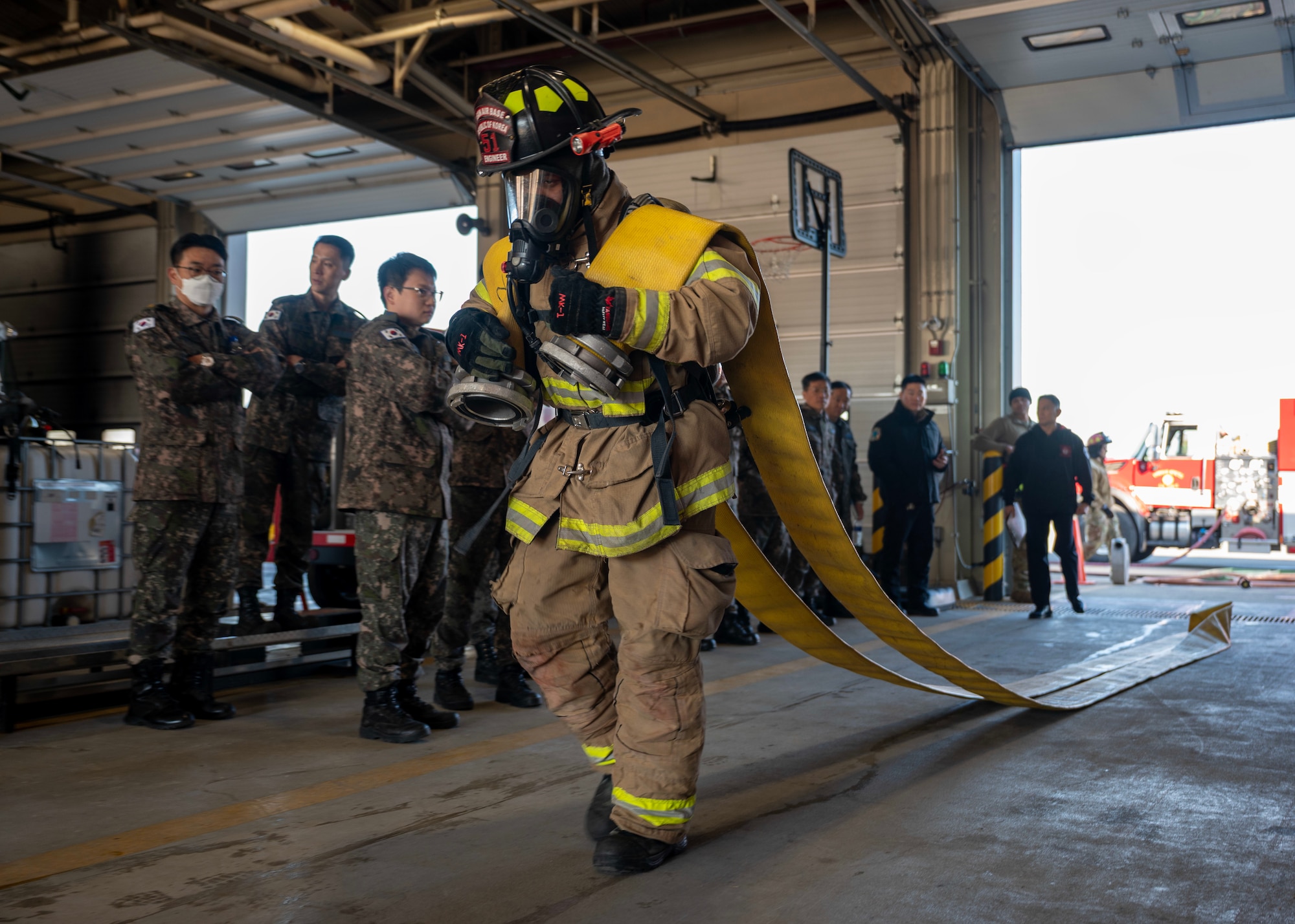 Participants of a joint fire training watch a hose drag at Osan Air Base, Republic of Korea, Nov. 21, 2025. U.S. firefighters demonstrated a physical training circuit that showcased the physical demands of fire protection. The event included hose carries, a dummy drag, ladder raises and climbs, and a Keiser sled strike. (U.S. Air Force photo by Staff Sgt. Sarah Williams)