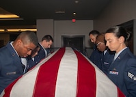 A photo of six Airmen holding up a casket.