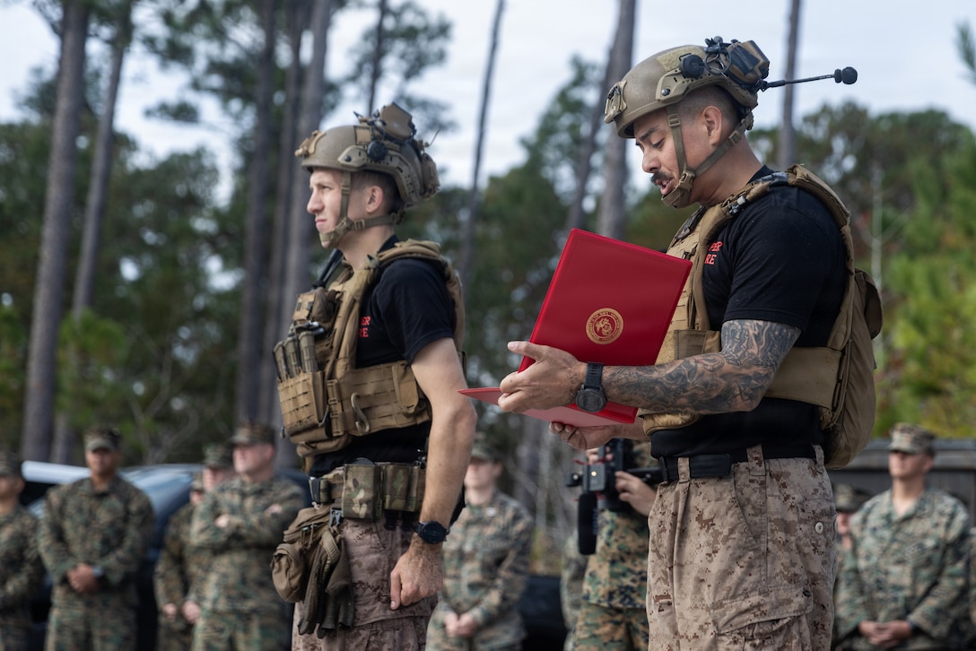U.S. Marine Corps Staff Sgt. Joseph Manzie, right, the staff-noncommissioned officer-in-charge of Sapper Leaders Course 1-26, reads a certificate of completion during the graduation ceremony of SLC 1-26 on Marine Corps Base Camp Lejeune, North Carolina, on Nov. 20, 2025. SLC is held to provide small unit leaders with 2d MARDIV the knowledge and ability to conduct squad level operations, increasing unit efficiency and warfighting capabilities. (U.S. Marine Corps photo by Cpl. Noelia Vazquez)