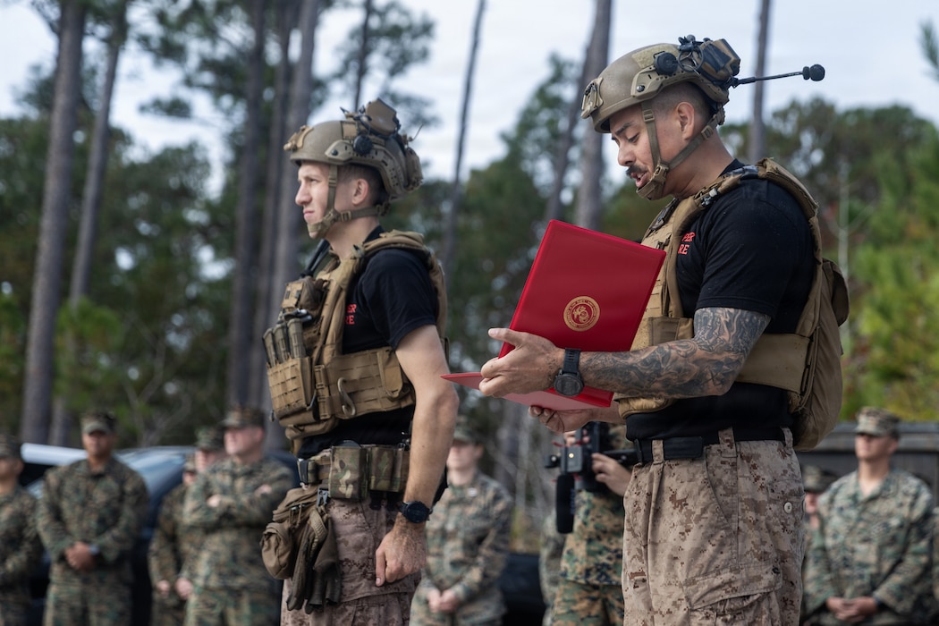 U.S. Marine Corps Staff Sgt. Joseph Manzie, right, the staff-noncommissioned officer-in-charge of Sapper Leaders Course 1-26, reads a certificate of completion during the graduation ceremony of SLC 1-26 on Marine Corps Base Camp Lejeune, North Carolina, on Nov. 20, 2025. SLC is held to provide small unit leaders with 2d MARDIV the knowledge and ability to conduct squad level operations, increasing unit efficiency and warfighting capabilities. (U.S. Marine Corps photo by Cpl. Noelia Vazquez)