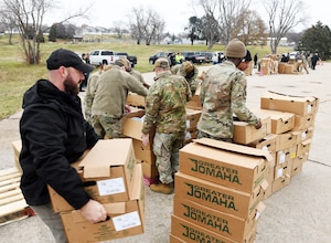 Uniformed military members stacking boxes in a parking lot.