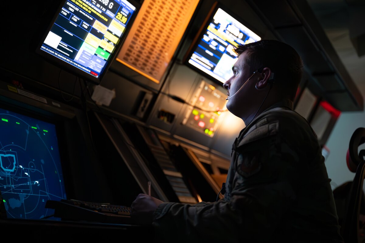 A man's face is illuminated as he stares at a screen while seated in a dark room.