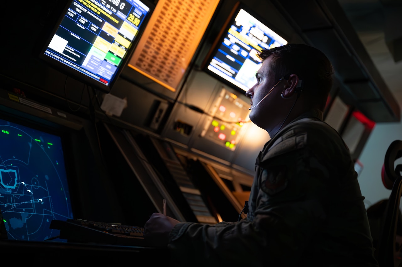 A man's face is illuminated as he stares at a screen while seated in a dark room.