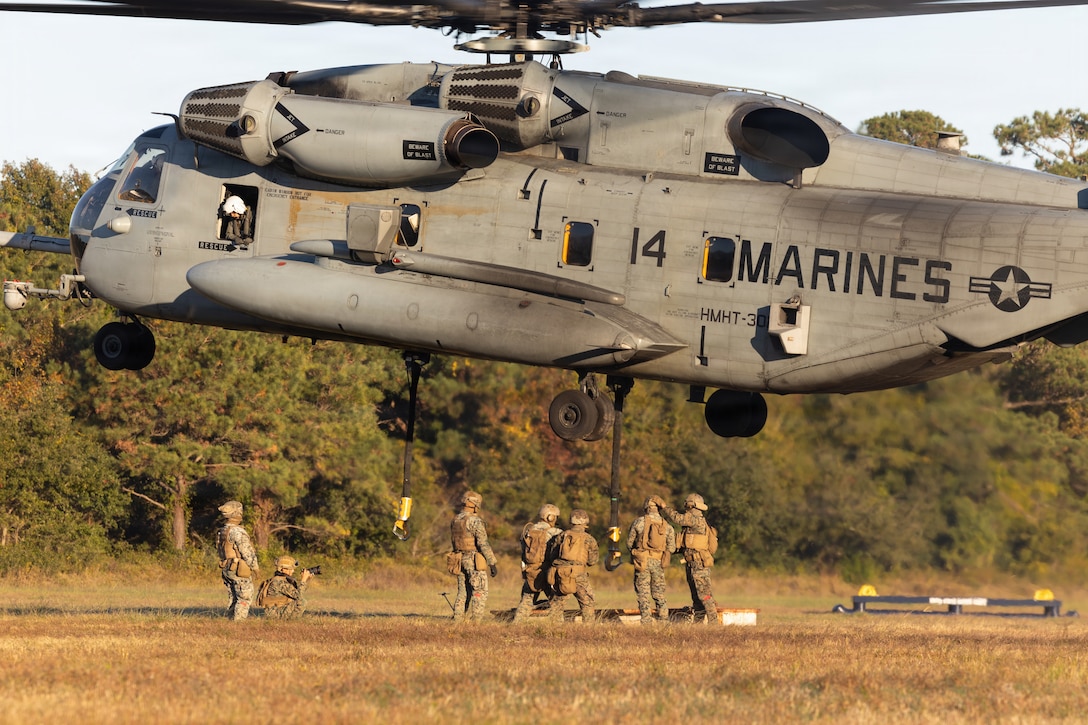 U.S. Marines with 2nd Distribution Support Battalion, Combat Logistics Regiment 2, 2nd Marine Logistics Group, attach a metal beam to a CH-53E super stallion assigned to Marine Heavy Helicopter Training Squadron 302, Marine Aircraft Group 29, 2nd Marine Aircraft Wing, during helicopter support team operations at Marine Corps Base Camp Lejeune, North Carolina, Nov. 4, 2025. 2nd DSB conducted the training to prepare Marines to manage lift operations at landing zones by facilitating the pickup, movement, and landing of helicopter-borne troops, equipment, and supplies. (U.S. Marine Corps photo by Lance Cpl. Isabelle Veillette)