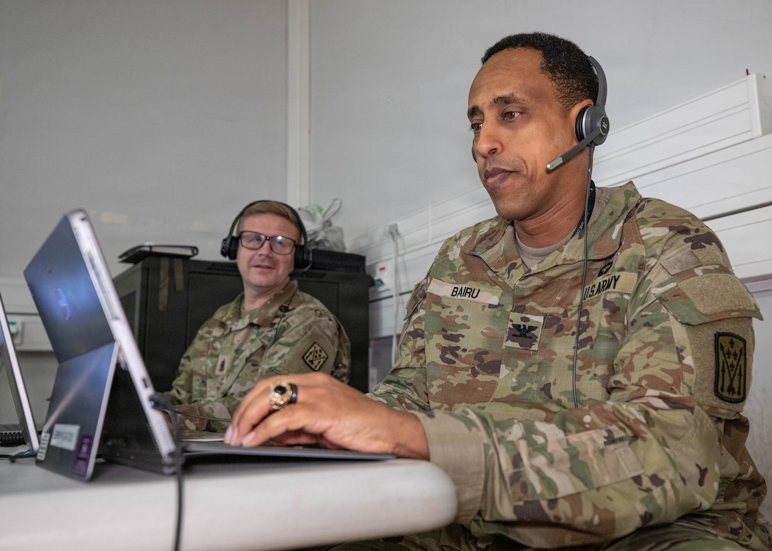 U.S. Army Col. Haileyesus Bairu, Commander of the 52nd Air Defense Artillery Brigade, listens to a Fires Support Element update brief in support of simulated V Corps operations with senior enlisted leader Paul Kenneth, left, Command Sgt. Maj. of the 52nd Air Defense Artillery Brigade, during Avenger Triad 25, Oct. 30, 2025, Camp Kosciuszko, Poland.