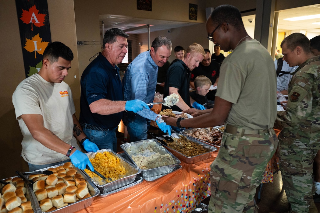 Tom Thompson, honorary commander and mayor of San Angelo; Jeremy Bartz, honorary commander alumni and local businessman; Lane Carter, honorary commander and county judge; and other volunteers serve food to military students at the Crossroads Student Ministry Center at Goodfellow Air Force Base, Texas, on November 21, 2025. This annual event is held with the intention of providing a warm Thanksgiving dinner to students who aren’t able to go home for the holidays. (U.S. Air Force photo by Airman 1st Class Maria Mota)