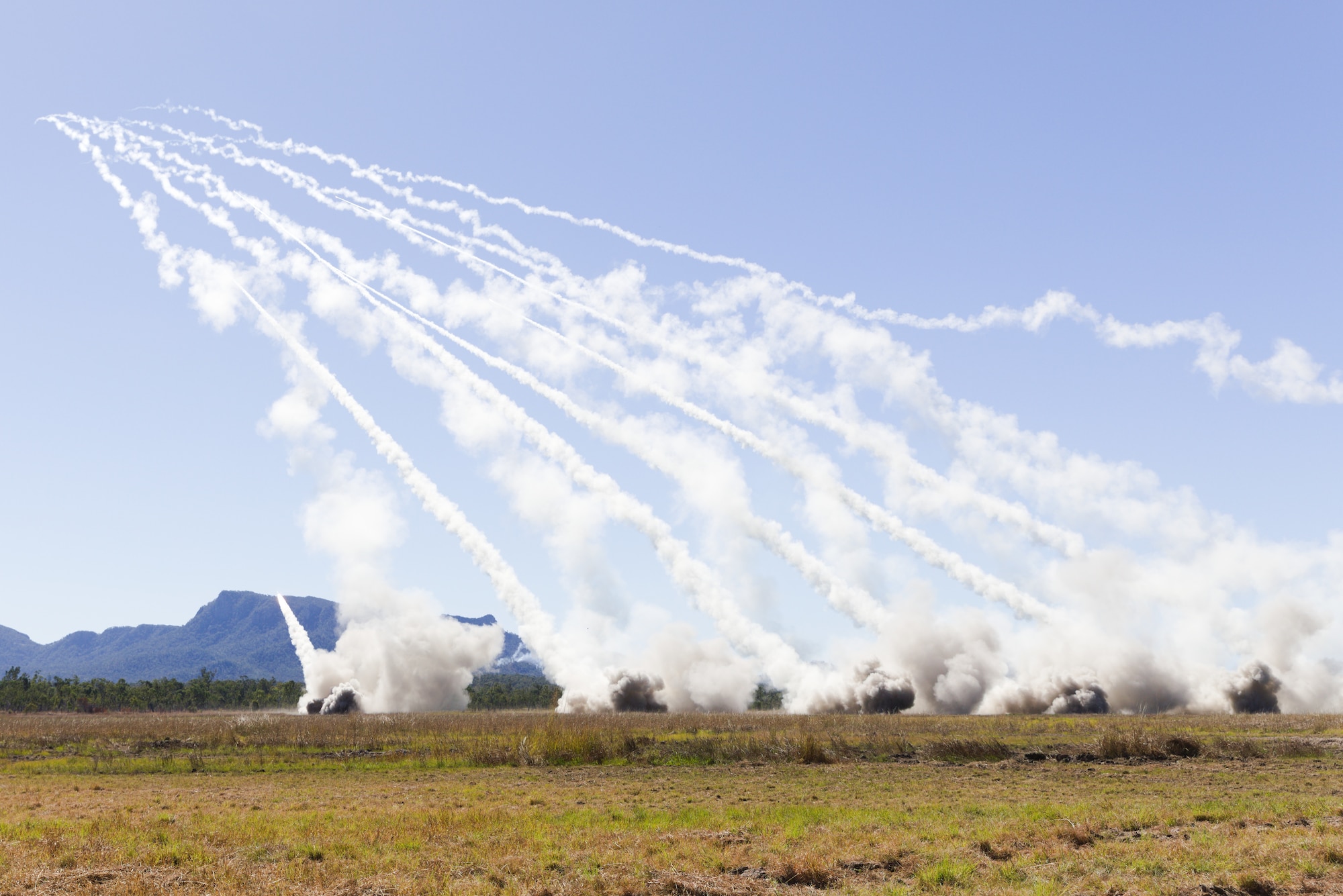 Plumes of smoke stretch to the left corner of the image, sticking out against the bright blue sky