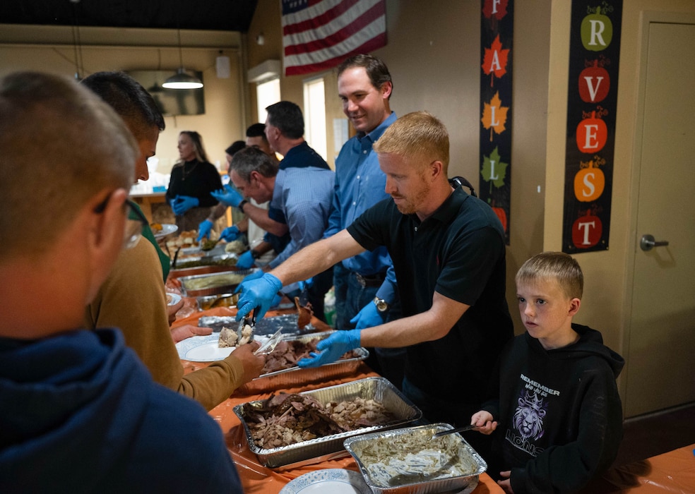 Trey Holmes, an honorary commander alumni and digital creator; Lane Carter, honorary commander and county Judge, and his son serve food to military students at the Crossroads Student Ministry Center at Goodfellow Air Force Base, Texas, Nov. 21, 2025. Every year, the community and leadership at Goodfellow AFB unite to prepare and serve a Thanksgiving meal to students from all branches of service. (U.S. Air Force photo by Airman 1st Class Maria Mota)