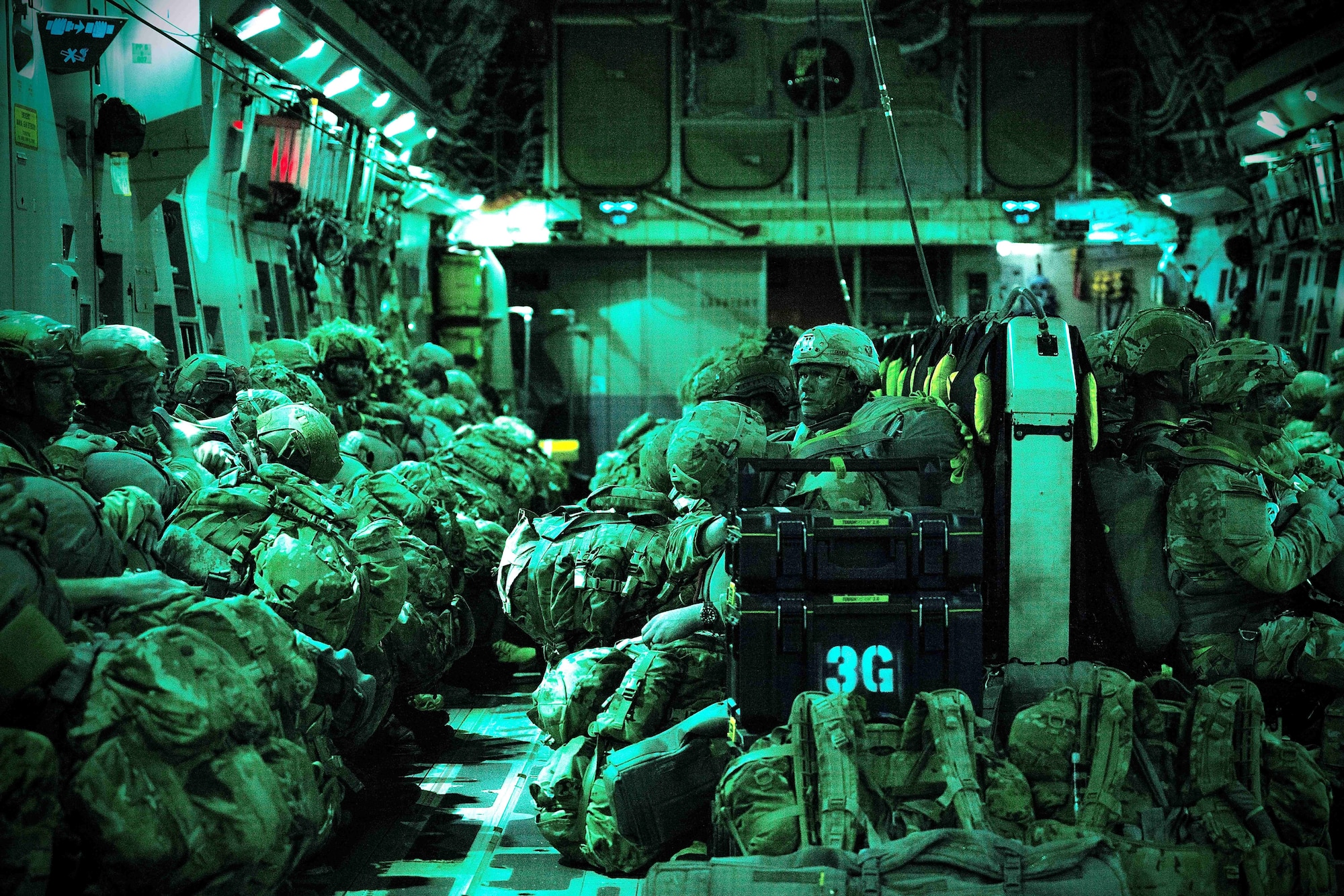 Soldiers in full kit sit in jump seats while a green light washes over them