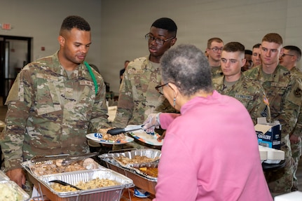 Retired U.S. Navy Cmdr. Patricia May, right, a volunteer and a member of the JBAB Chapel congregation, places food on the plate of U.S. Air Force Airman 1st Class Keagan Pace, left, a U.S. Air Force Honor Guard technical school trainee, at Joint Base Anacostia-Bolling, Washington, D.C., Nov. 26, 2025. Single service members enjoyed a special meal served by their leadership, aimed to create cherished memories and strengthen the bonds that define their shared commitment to duty and service. (U.S. Air Force photo by Hayden Hallman)