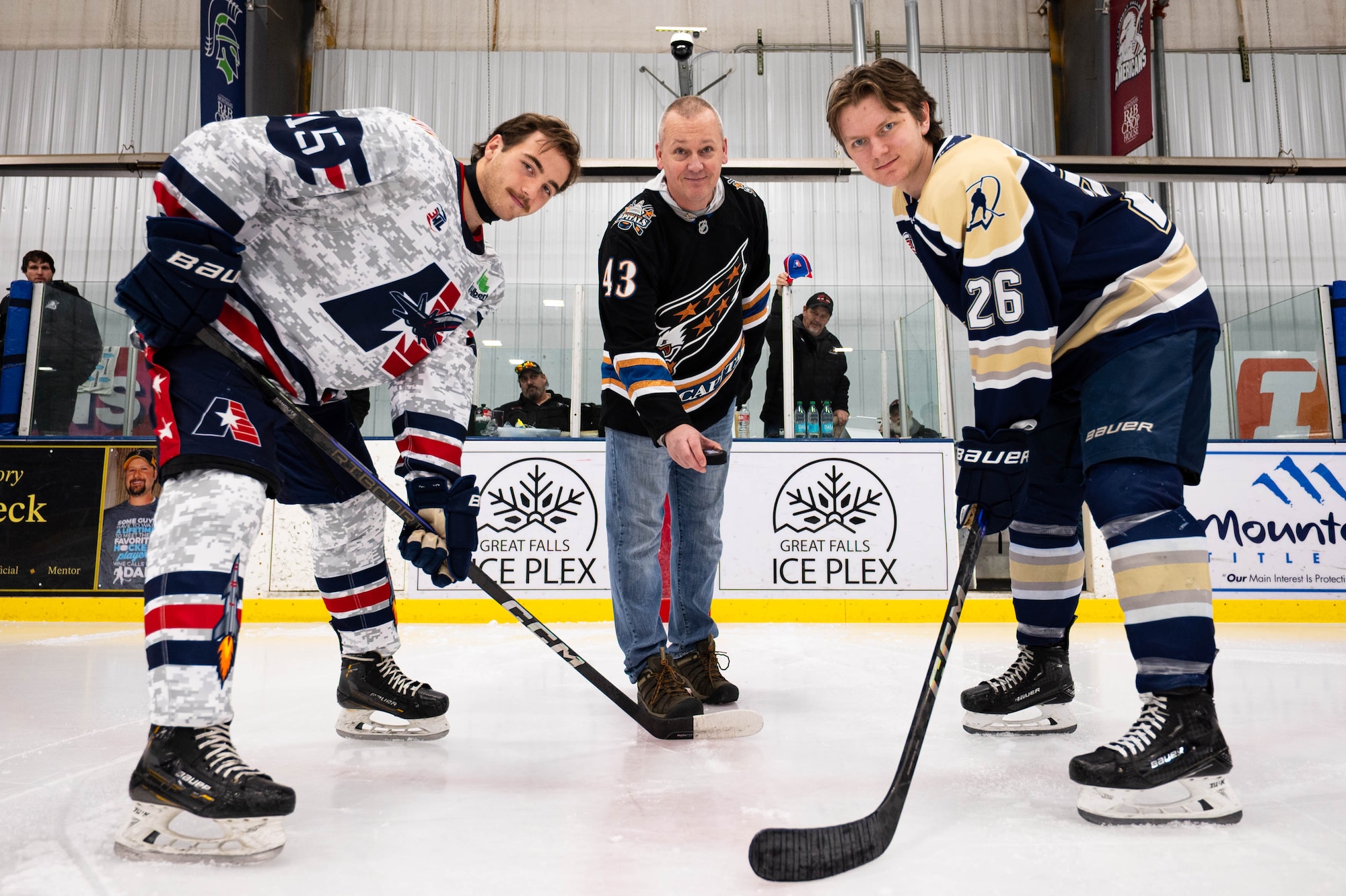 A man in civilian attire holds a hockey puck in between two men in hockey jerseys.