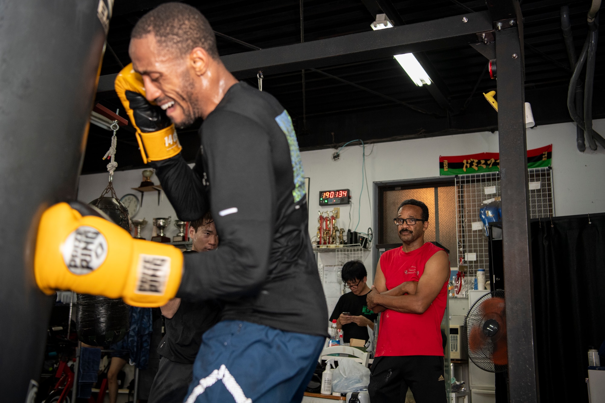 Rick Yoshimura watches U.S. Air Force Senior Airman Craig Jeudy, Fifth Air Force technical support technician, complete a punching bag drill during a training session.